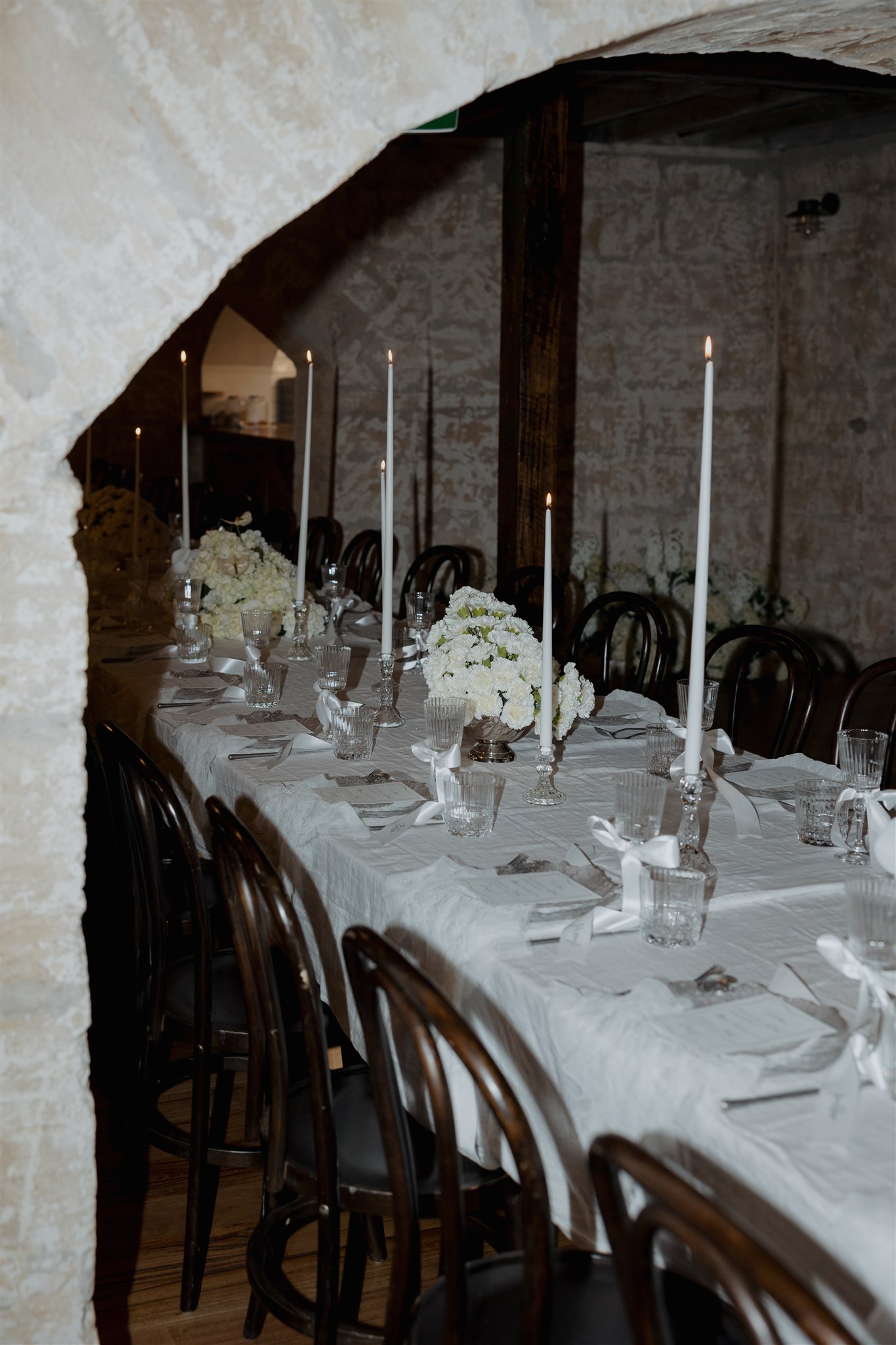 Elegant tablescape featuring pearl-themed accents, premium linens, and vintage tableware at Lauren and Bernie’s romantic intimate wedding reception at Frolic Lane, showcasing rustic sandstone arches in the background. 35mm film wedding photography.